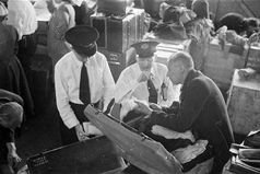 1950: Ellis Island immigration officers check the luggage of passengers from the last European displaced persons boat. (Credit: Ernst Haas/Getty Images)